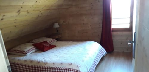 Chambre cosy du chalet en bois aux Chalets Cocody, Jausiers, avec lit, oreillers à carreaux et vue montagne par la fenêtre