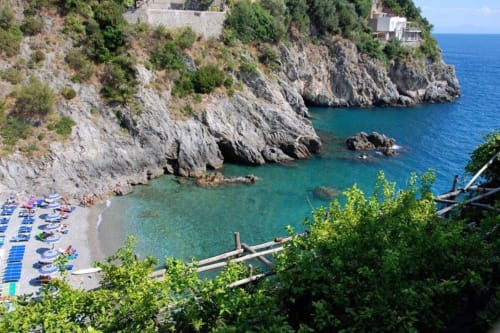 Spiaggia di una caletta esclusiva a Villa Costanza sulla Costiera Amalfitana con acque cristalline, scogliere calcaree e lettini presso Maiori