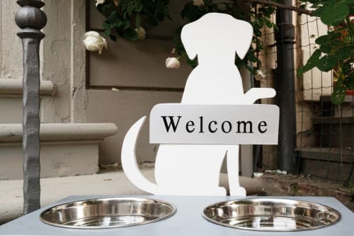 Cartello di benvenuto a forma di cane presso Casa Mirko, B&B ad Arezzo, con ciotole vuote per il cibo
