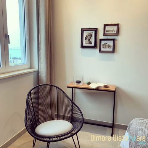 Accogliente angolo lettura con poltrona in vimini nera, scrivania e finestra con vista mare a B&B Dimora Vistamare a Barletta