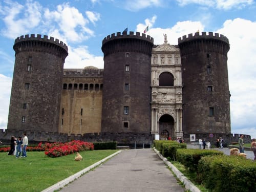 Castel Nuovo, fortezza medievale di Napoli con torri merlate, arco d'ingresso ornato e ampi giardini verdi