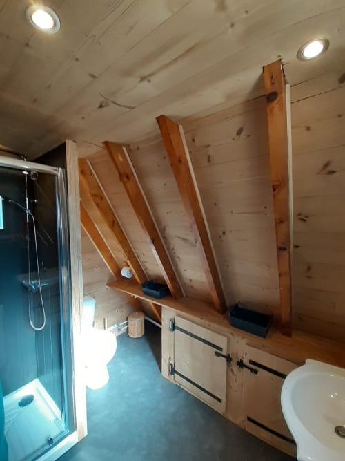 Salle de bains moderne du Chalet Cocody à Jausiers avec étagères en bois, douche, toilettes et chauffage au sol