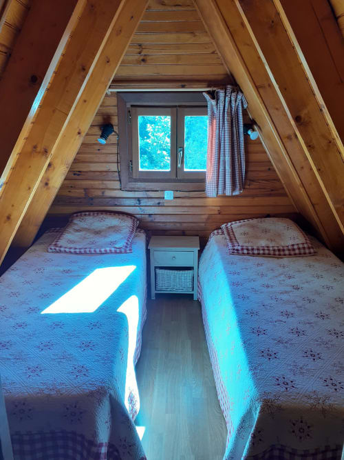 Chambre cosy en chalet A avec deux lits jumeaux, poutres en bois et vue sur les montagnes par la fenêtre
