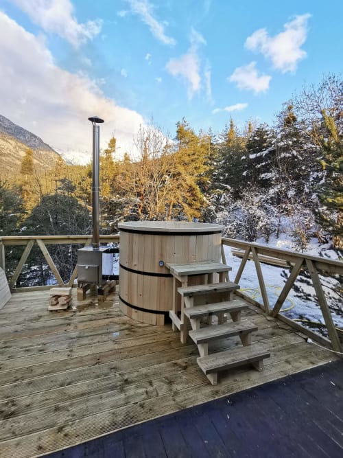Bain à remous en bois avec escaliers sur une terrasse surplombant les montagnes enneigées des Chalets Cocody à Jausiers, France