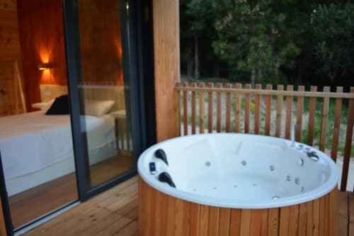 Bañera de hidromasaje al aire libre en terraza de madera con vistas al dormitorio en Cabañas Compostela, Santiago de Compostela