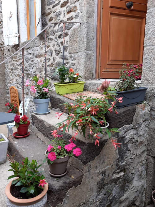 Entrée en pierre avec fleurs en pots colorés au gîte Le refuge des Alpes mancelles à Fresnay-sur-Sarthe