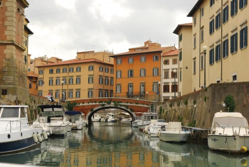Suggestivo canale toscano con barche ormeggiate, edifici colorati e ponte ad arco vicino a Pomarance