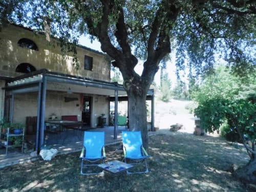 Lettini blu sotto albero secolare presso Agri-Bio Santa Palmira a Pomarance, Italia, con edificio in pietra