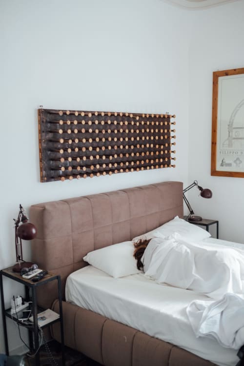 Letto rivestito in beige con biancheria bianca presso Sicilianinsta Rooms, Catania. Visibili decorazione murale in legno e lampada da comodino.