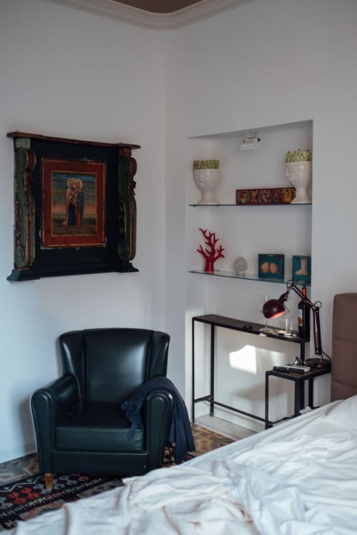 Camera moderna di Sicilianinsta Rooms a Catania con poltrona in pelle nera, scrivania, ripiani, opere d'arte religiosa e arredamento bianco