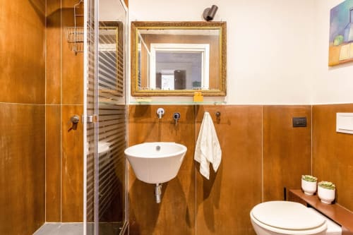 Bagno moderno presso Sicilianinsta Rooms Catania con piastrelle arancioni, lavabo bianco, WC, doccia e scaldasalviette