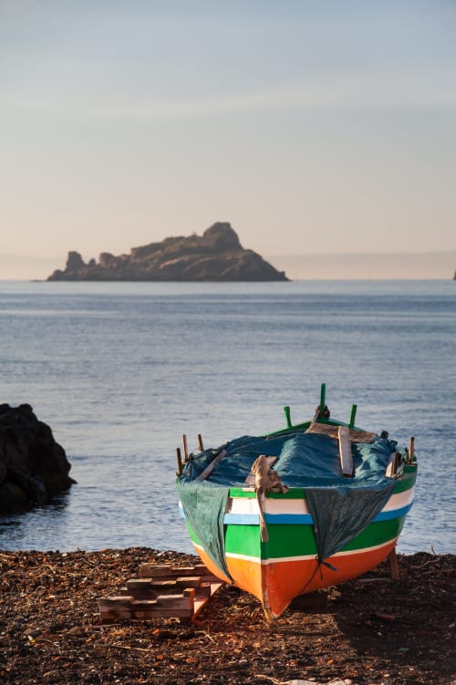 Colorata barca da pesca sulla spiaggia di Catania con isola rocciosa in lontananza, Sicilia