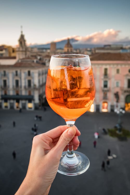 Mano che sorregge un aperitivo con vista sulla storica piazza di Catania, Sicilianinsta Rooms
