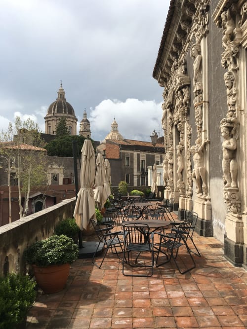 Terrazza elegante delle Sicilianinsta Rooms a Catania con architettura barocca, tavoli da pranzo e vista della cupola della cattedrale