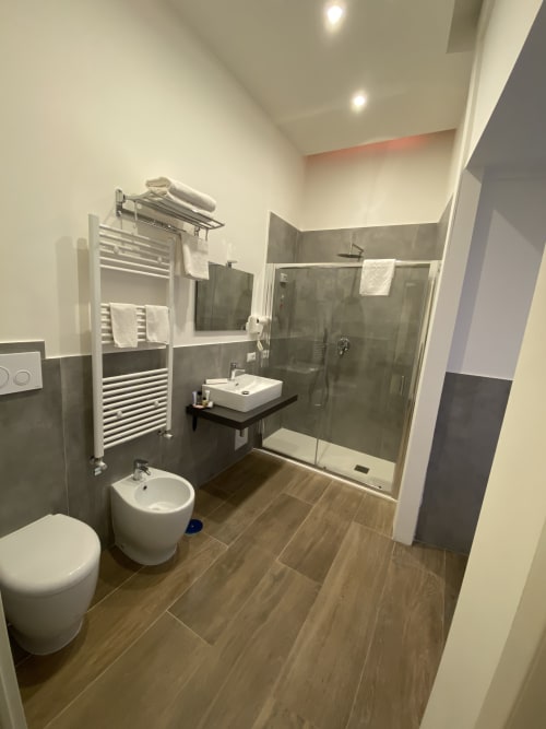 Modernes Badezimmer in der Luxussuite Salotto Toledo in Neapel mit großzügiger Dusche, weißen Armaturen und Holzoptik-Bodenbelag
