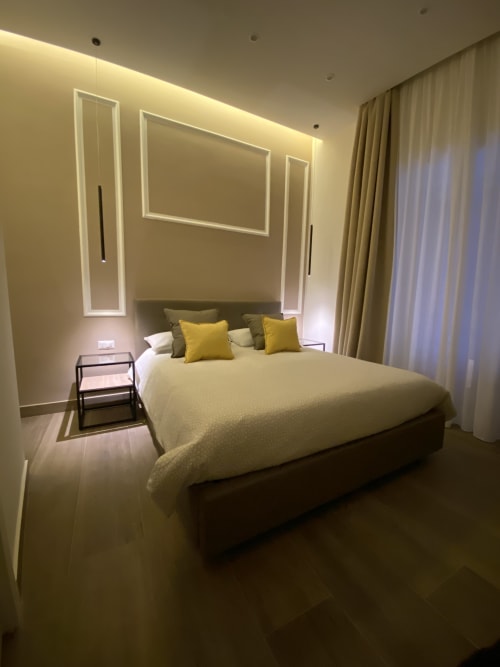 Modernes Luxusschlafzimmer im Salotto Toledo Neapel mit Queensize-Bett, LED-Akzentbeleuchtung, gelben Kissen und raumhohen Fenstern