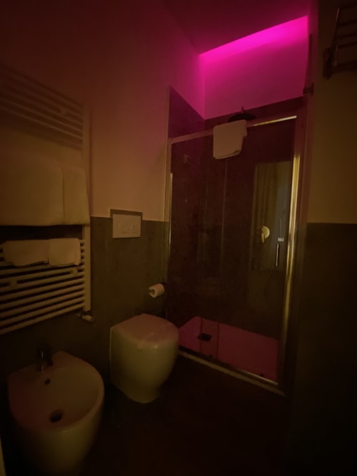Modernes Badezimmer im Salotto Toledo, Luxuszimmer in Neapel, mit rosa Neonbeleuchtung an der Decke, gläserner Dusche und
