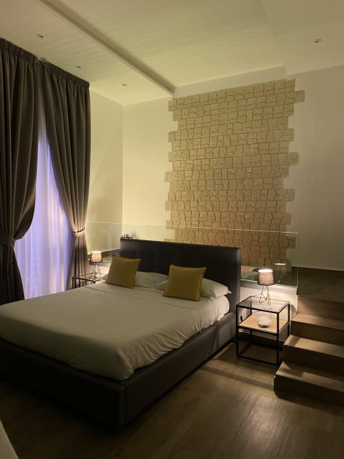 Modernes Luxus-Schlafzimmer im Salotto Toledo Neapel mit schwarzem Bett, strukturierter Steinakzentwand und Umgebungsbeleuchtung