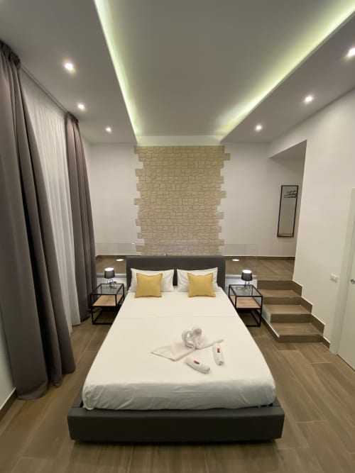 Luxuszimmer im Salotto Toledo Neapel mit moderner Deckenbeleuchtung, cremefarbener Backsteinakzentwand und hochwertiger Bettwäsche