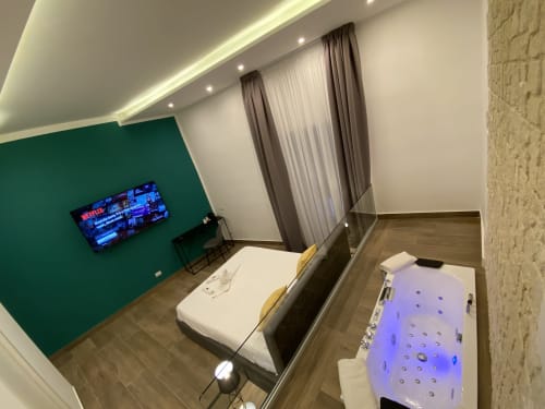 Modernes Luxuszimmer im Salotto Toledo Neapel mit grüner Akzentwand, Flachbildfernseher, Bett und beleuchtetem Whirlpool