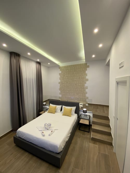 Modernes Luxusschlafzimmer im Salotto Toledo Neapel mit schwarzem Bett, gelben Akzenten, Backsteinmauer und Umgebungslicht