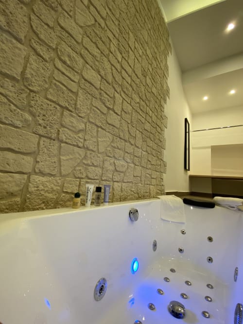 Luxus-Whirlpool-Badewanne mit blauer Beleuchtung und Steinakzentwand in einer Suite des Boutique-Hotels in Neapel