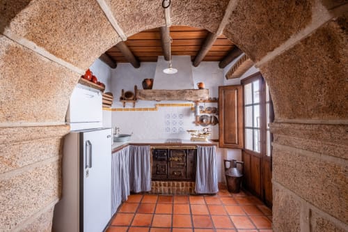 Cocina rústica en Casa Rural El Fontano de Montánchez con paredes de corcho, vigas de madera, suelo de barro y estilo tradicional