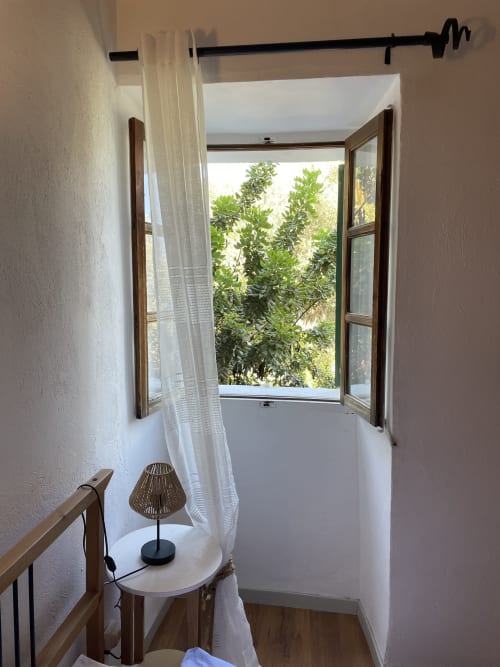 Bright balcony with open wooden doors, white curtains, small table with lamp, and green garden views at Petit Hotel Sa Plana,
