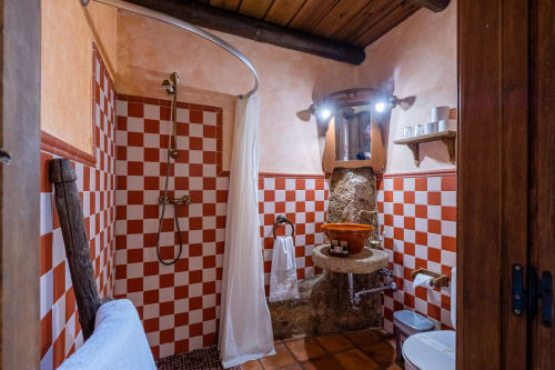 Baño rústico con azulejos a cuadros rojo y blanco, lavamanos de piedra y vigas de madera en Casa Rural El Fontano, Montánchez