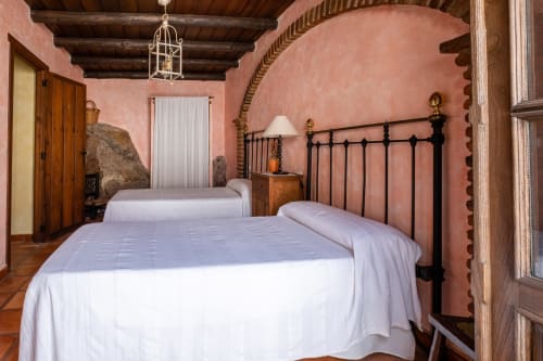 Dormitorio rústico en Casa Rural El Fontano con camas gemelas, cabeceros de hierro, paredes de terracota, vigas de madera oscura y decoración tradicional