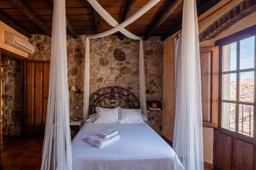 Habitación rústica de piedra con cama dosel blanca en Casa Rural El Fontano en Montánchez