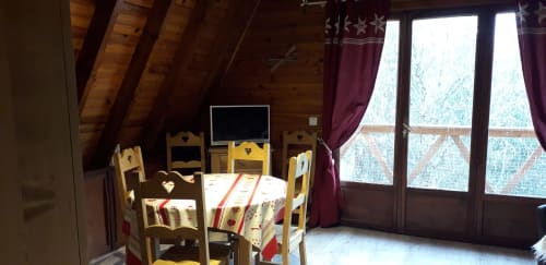 Salle à manger rustique à la villa Chalets Cocody avec chaises en bois, vue montagne par les portes-fenêtres et paysage enneigé