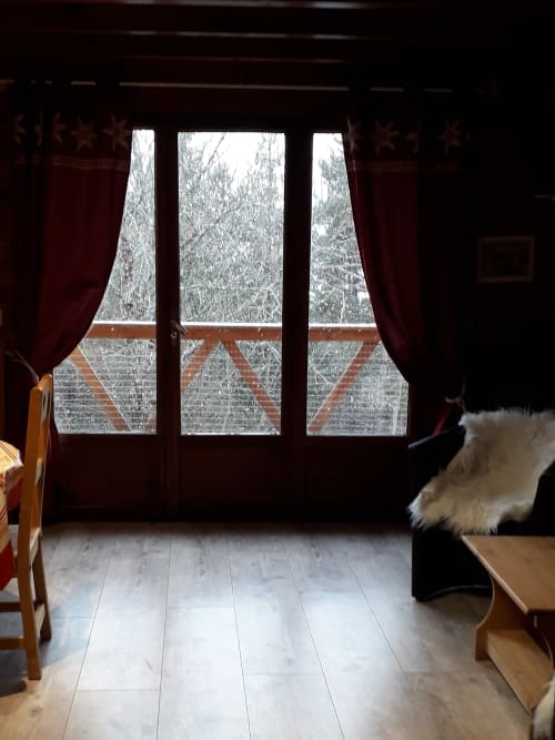 Vue enneigée de la montagne depuis le Chalet Cocody Montagnard à Jausiers, avec portes en bois, rideaux rouges et salle à manger.