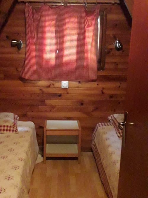 Intérieur rustique de chalet avec lits jumeaux, rideaux à carreaux rouges et ambiance de refuge montagnard aux Chalets Cocody