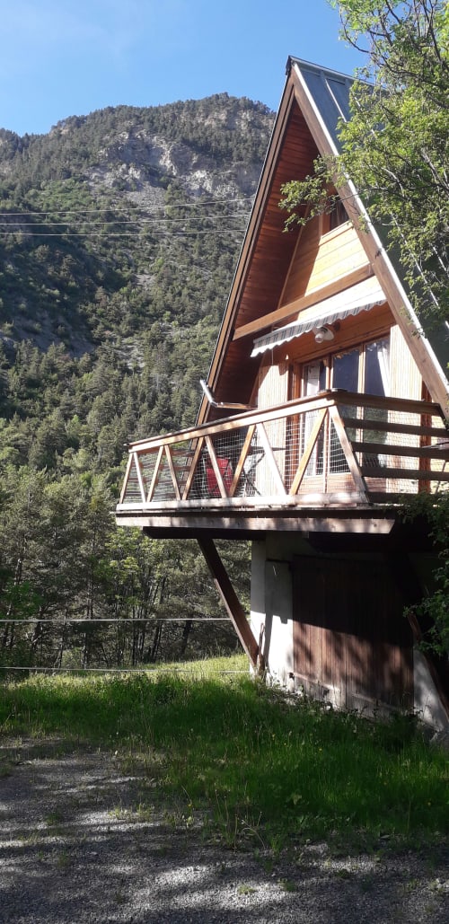 Chalet moderne en A dans les montagnes de Jausiers avec terrasse en bois et balustrade surplombant une vallée forestière