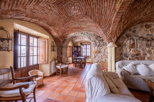 Rustic villa bedroom at Casa Rural El Fontano with arched brick ceilings, terracotta floors, stone walls, and white bedding