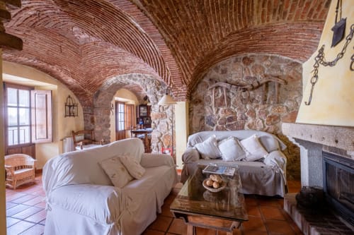 Rustic stone villa interior at Casa Rural El Fontano with vaulted brick ceilings, cream sofas, fireplace, and traditional