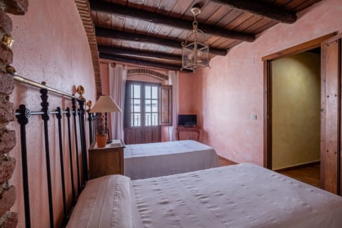Bedroom at Casa Rural El Fontano villa in Montanchez with twin beds, wrought iron headboards, and pink terracotta walls
