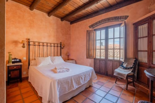 Rustic bedroom at Casa Rural El Fontano in Montanchez with terracotta walls, wooden beams, and balcony views
