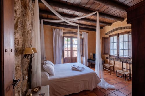 Elegant canopy bed in Casa Rural El Fontano villa, Montanchez, with terracotta floors, cream drapes, and arched windows