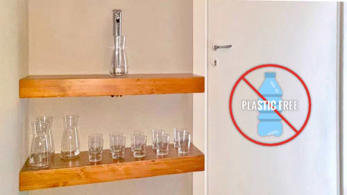 La guest house Casa Mirko ad Arezzo espone bicchieri su scaffali di legno con cartello di certificazione plastic-free in parete