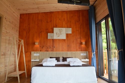 Dormitorio moderno en Cabañas Compostela con pared de madera, ropa de cama blanca y acceso a terraza en Santiago de Compostela