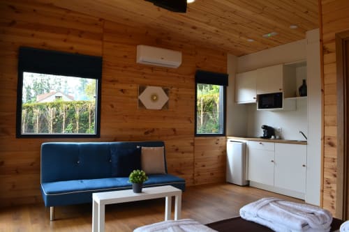 Moderno apartamento de cabaña de madera en Cabañas Compostela con sofá azul, cocineta y vistas al jardín