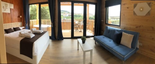 Dormitorio moderno en Cabañas Compostela con vistas a la ciudad, cama, sofá, detalles en madera y acceso a terraza