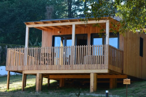 Cabaña de madera elevada con terraza cubierta y barandilla con vistas al bosque en Cabañas Compostela