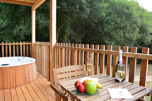 Terraza de madera en Cabañas Compostela con jacuzzi, banco de comedor, tabla de frutas, vino y copas con vistas al bosque