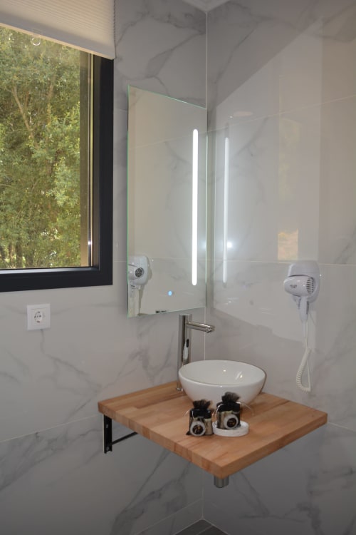 Baño moderno en Cabana A Fervenza con paredes de mármol, lavamanos de cerámica, espejo iluminado, tocador de madera y vistas a la montaña