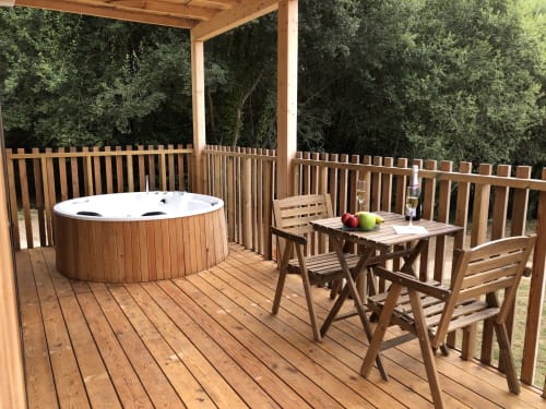 Terraza de madera con bañera de agua caliente y zona de comedor con vistas al bosque, Cabañas Compostela