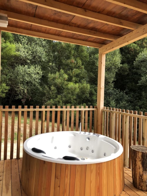 Bañera de hidromasaje al aire libre en terraza de madera en Cabañas Compostela con vistas al bosque y pérgola