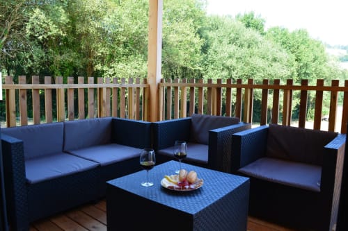 Terraza de madera en Cabañas Compostela con muebles de ratán negro, cojines azules, vistas a la montaña y árboles verdes